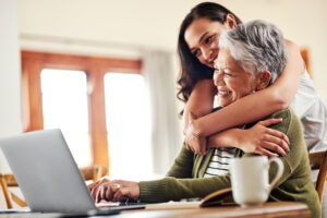 daugher hugging mother looking at laptop while discussing reverse mortgages